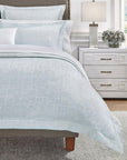 The corner of a bed with the SFERRA Graticcio Duvet Cover in pale blue with pillows and shams.
