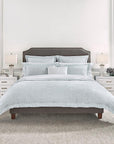A brown bed in a white bedroom with a pale blue SFERRA Graticcio bedding set.