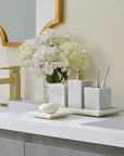 A bathroom counter with grey marble SFERRA Pietra bathroom accessories and white hydrangeas.