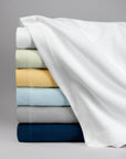 Stack image of navy, grey, light blue, yellow, light green, and white Allegra blankets against a grey background.