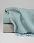 Stack image of the basketweave Palmilla throw in blue and grey against a grey background.