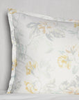 Corner shot of a white cotton sham with a light yellow floral motif against a white background.