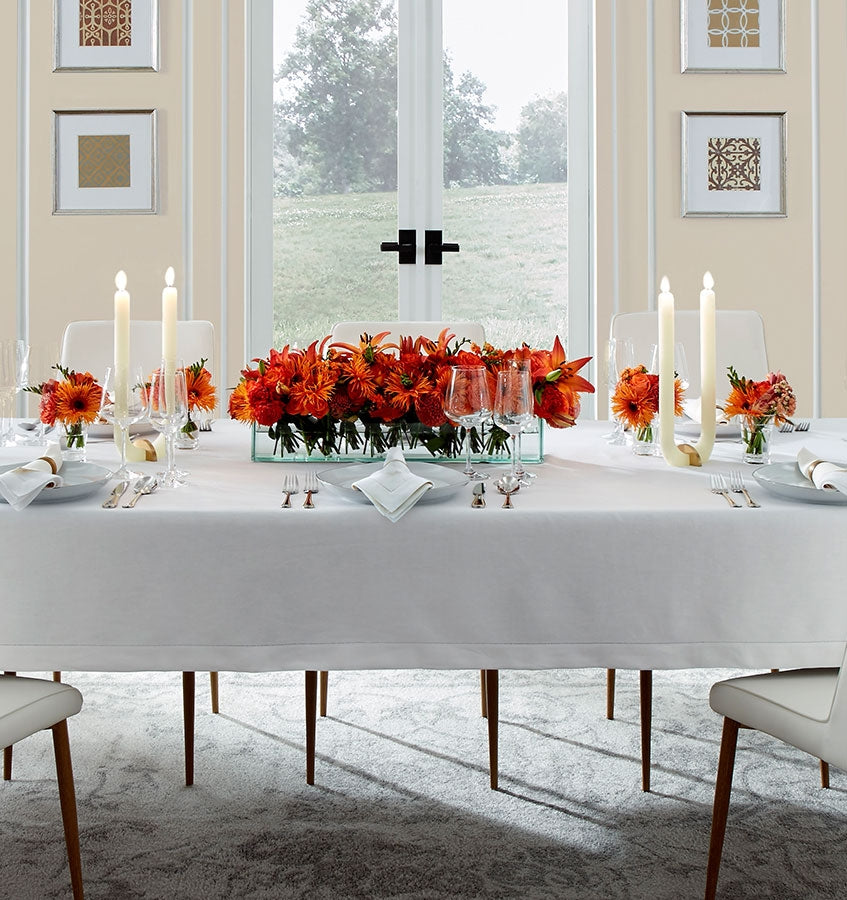 A table with orange flowers set with the SFERRA Classico fine linen table collection.