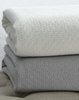 The SFERRA Corino lightweight, breathable cotton blanket in white, ivory, seagreen, and powder blue.