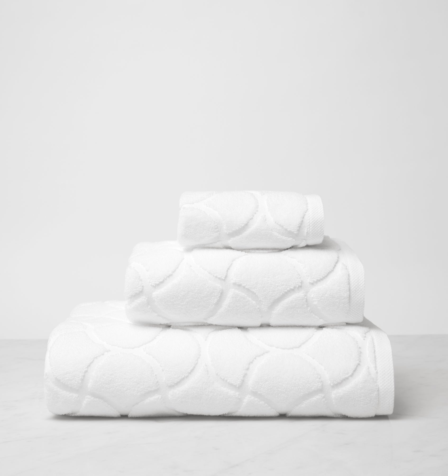 Oasi white bath towels side view stacked, top to bottom: washcloth, hand towel, bath towel. 