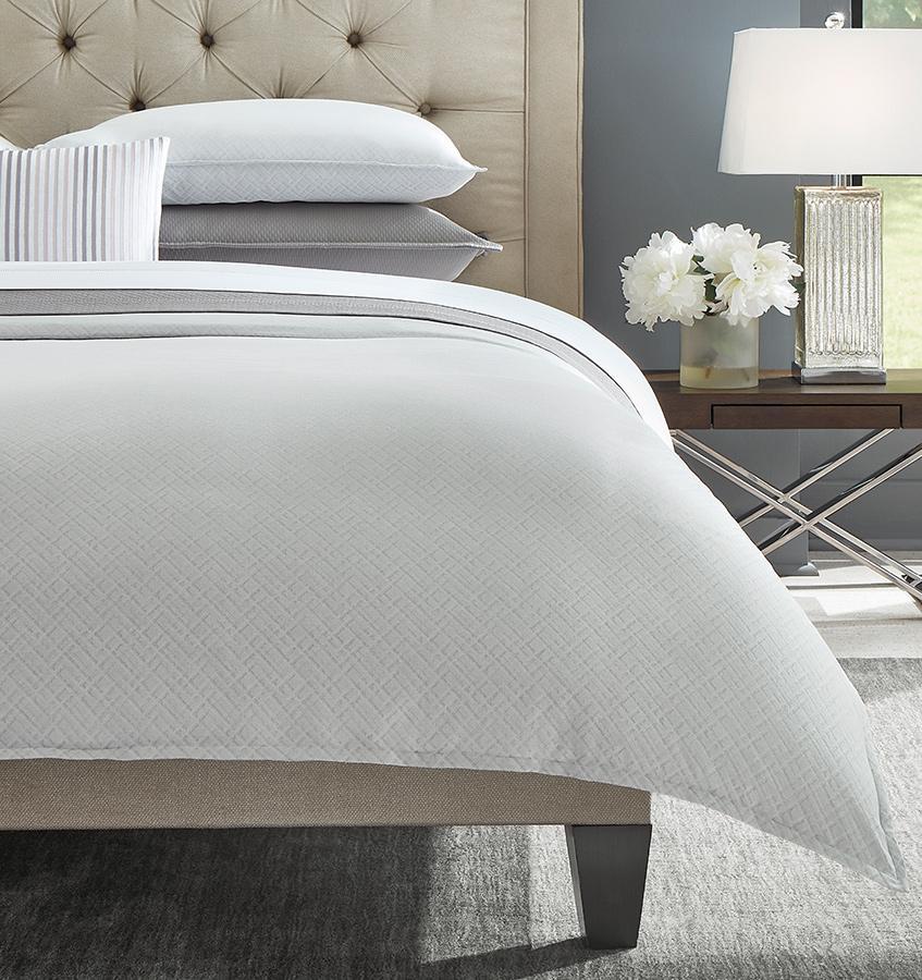 The left corner of a grey SFERRA Abriana Duvet Cover with shams and a striped decorative pillow.