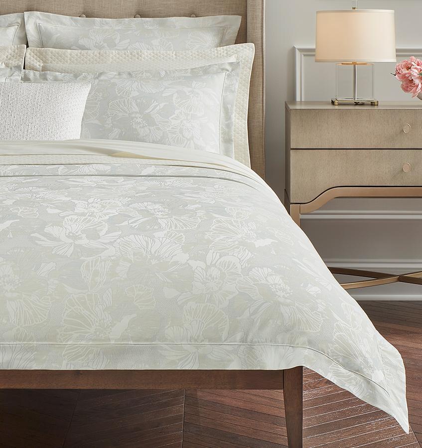 The corner of a bed with the SFERRA Fiore Duvet Cover in pale green with a floral jacquard pattern.