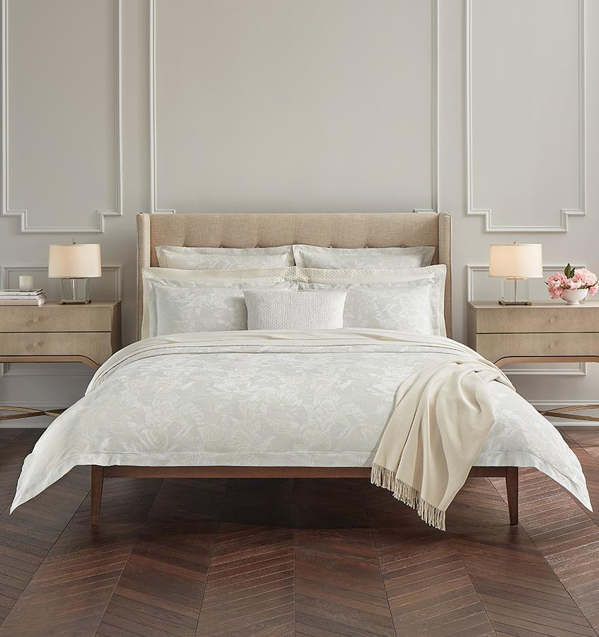 A bed with SFERRA Fiore Duvet Cover, pillows, shams, a decorative pillow and a fringed throw.