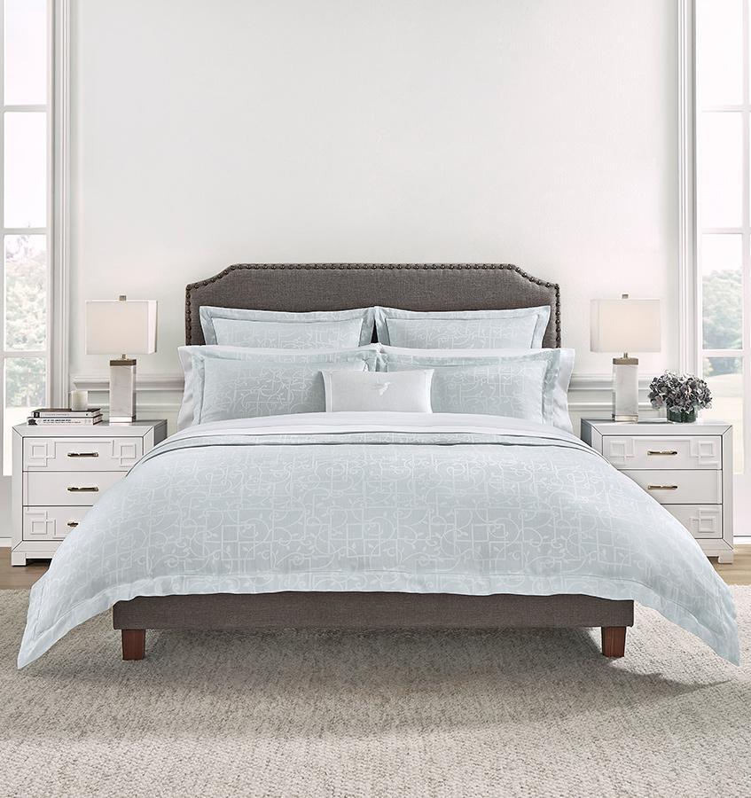 A brown bed in a white bedroom with a pale blue SFERRA Graticcio bedding set.