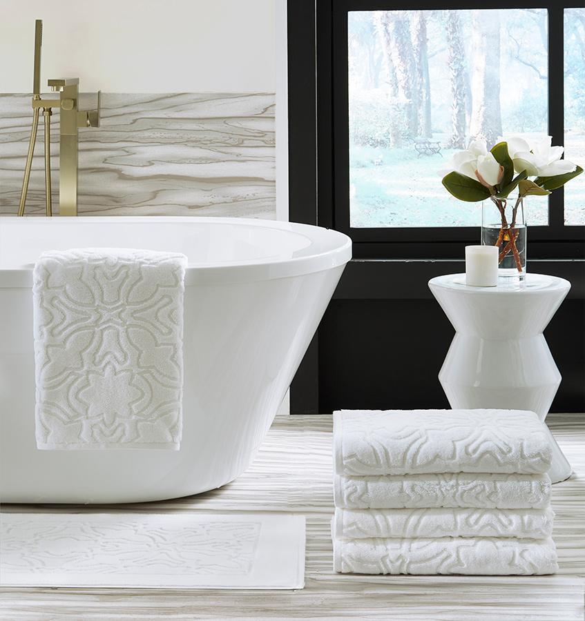 Bath tub with a SFERRA sculpted jacquard towel draped over the side with a stack of towels next to the bath.