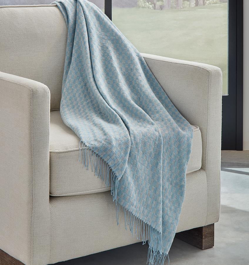 SFERRA Palmilla throw in blue draped over a beige armchair. 