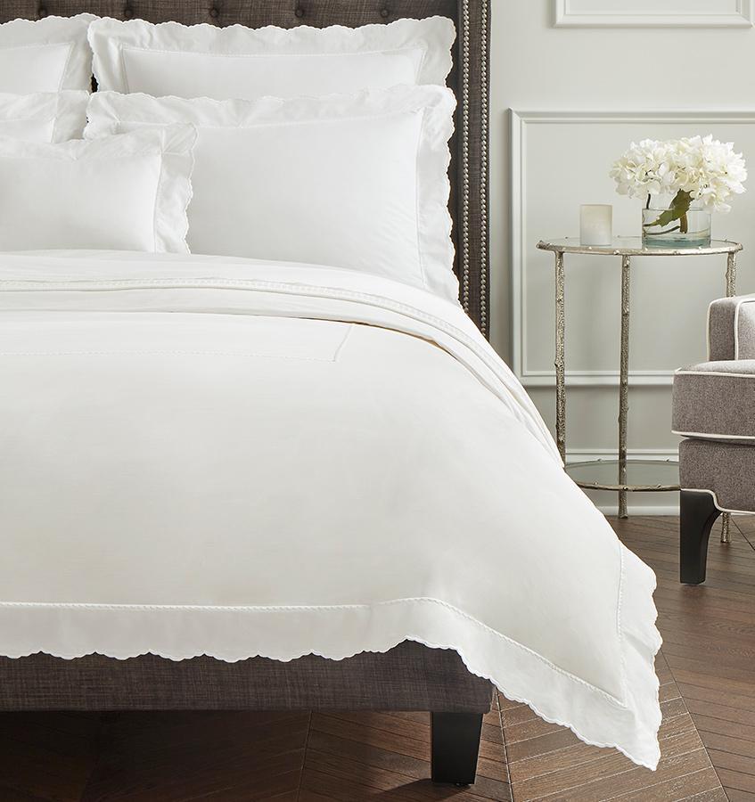 A brown bed with all-white SFERRA Pettine sheets with white scalloped edges.