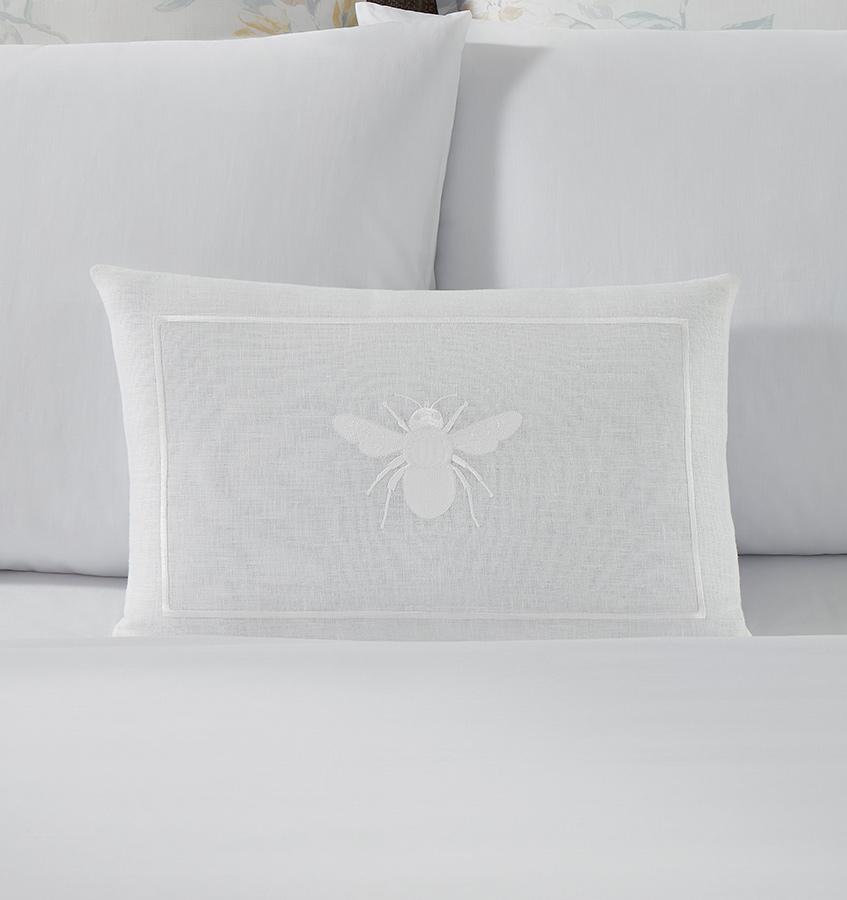A white linen SFERRA decorative pillow with a white embroidered bee.
