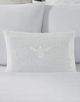 A white linen SFERRA decorative pillow with a white embroidered bee.