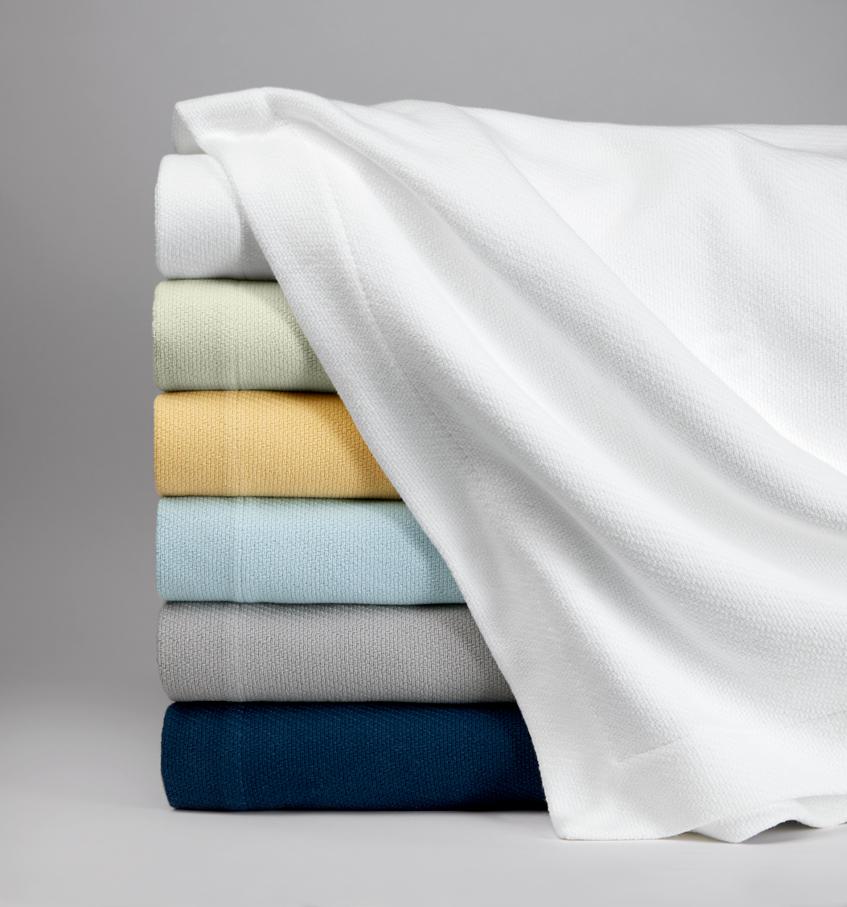 Stack image of navy, grey, light blue, yellow, light green, and white Allegra blankets against a grey background.