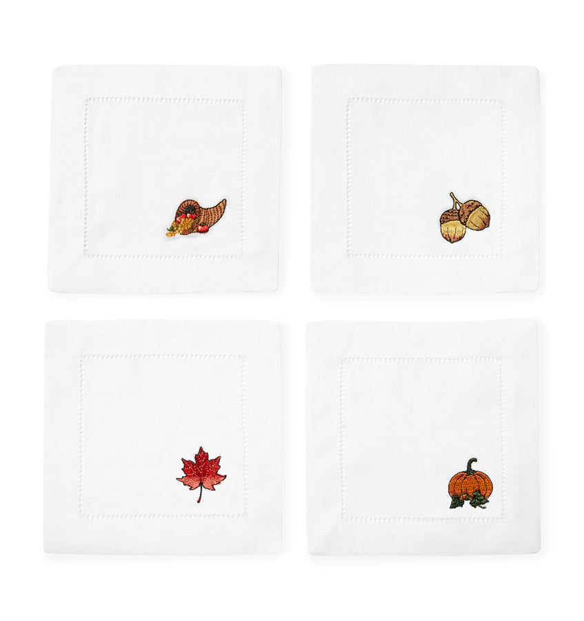 SFERRA Autunno Cocktail Napkins feature fall motifs of an acorn, cornucopia, maple leaf, and pumpkin embroidered on linen napkins.