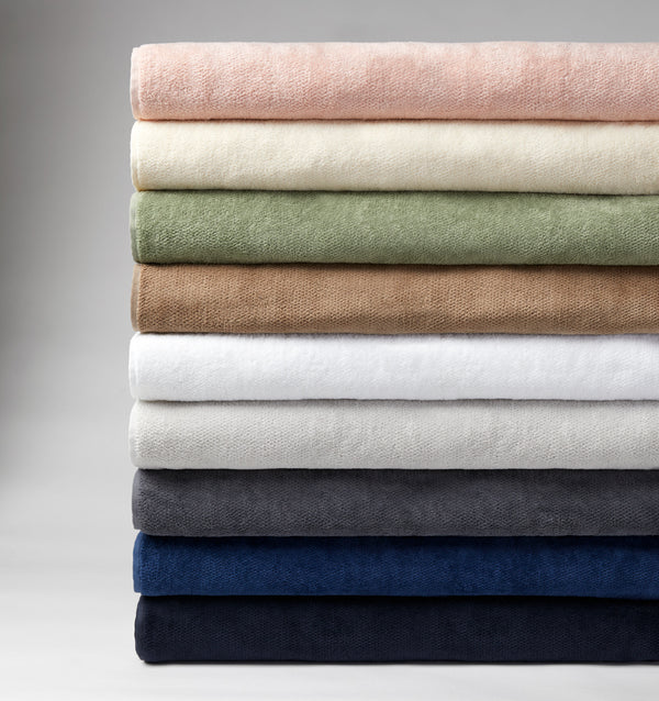 A stack of 9 colors of SFERRA plush luxury bath towels against a grey background.