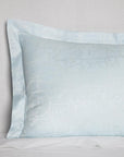 Corner shot of a light blue sateen sham woven with a white trellis pattern against a white background.