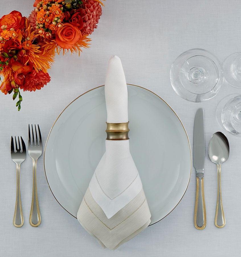The SFERRA Classico fine linen napkin wrapped with a napkin ring sitting on a table setting.