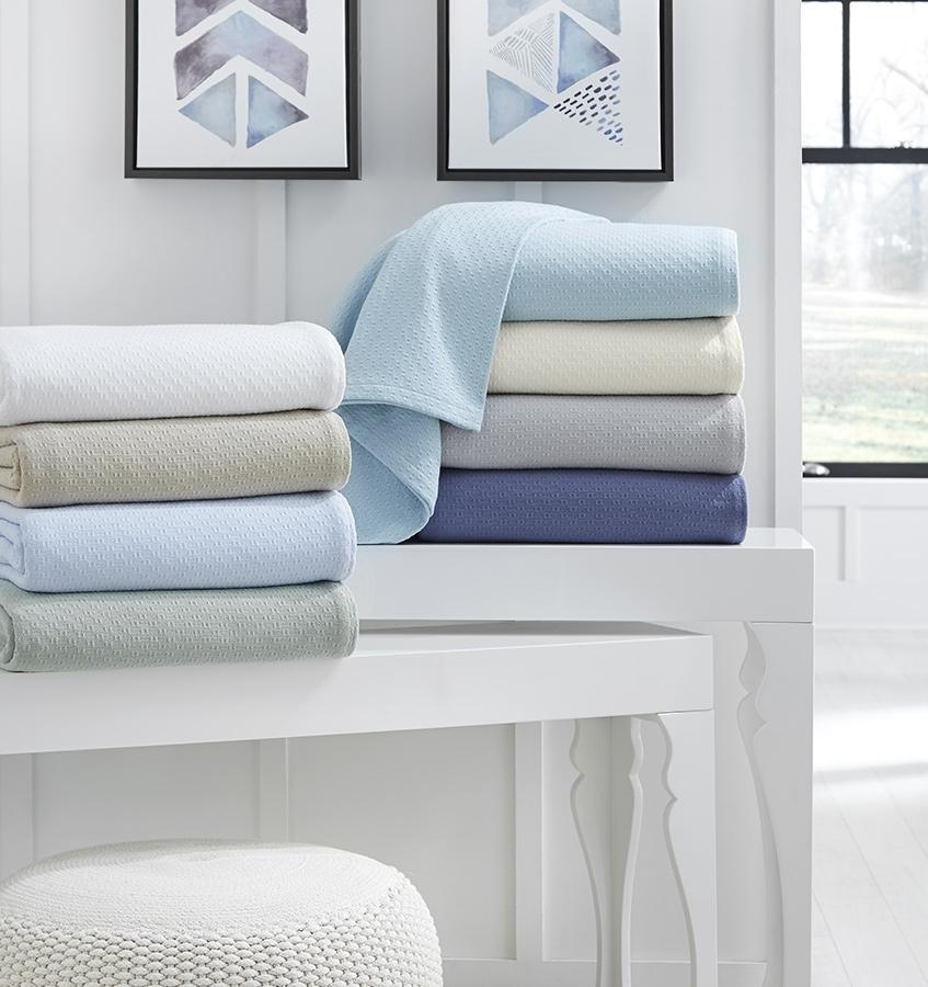 The SFERRA Corino lightweight, breathable cotton blanket in white, ivory, seagreen, and powder blue.