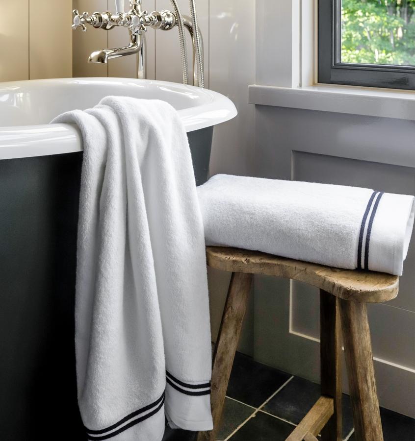 SFERRA Aura bath towels with multi-colored embroidered striped borders draped over a bath tub.