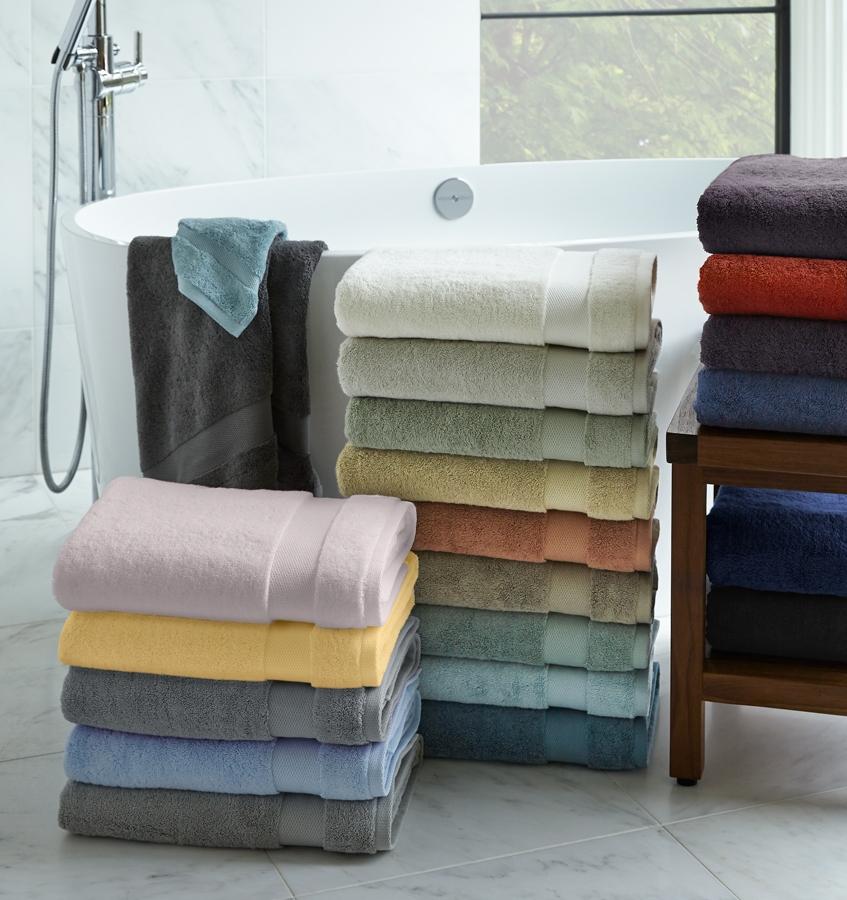 Stacks of plush cotton SFERRA Bello bath towels on a bathroom floor.