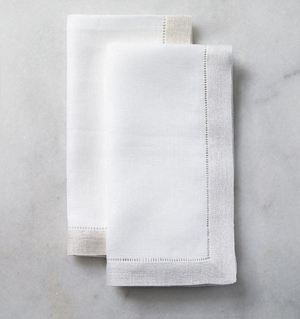 Two folded SFERRA Filetto dinner napkins against a white marble background.