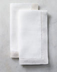 Two folded SFERRA Filetto dinner napkins against a white marble background.