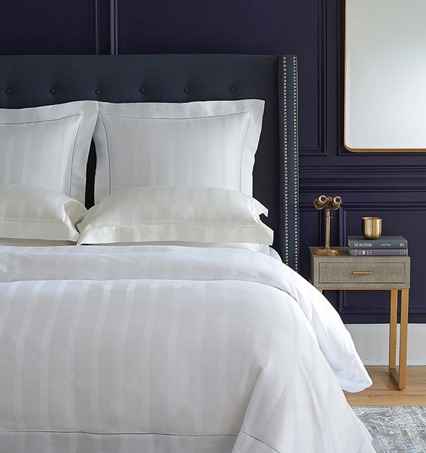 A bed with SFERRa Giza 45 Stripe bedding, crafted from the finest cotton in the world.